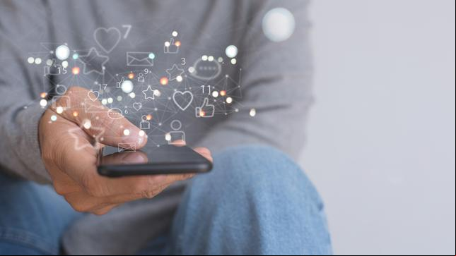Bild: iStock / Getty Images Plus/Tippapatt Mann, der das Mobiltelefon zu Hause mit Social-Media-Apps-Symbolen auf dem virtuellen Bildschirm