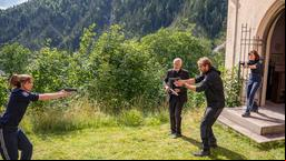 Der Pfarrer (Frank Leo Schröder) und sein Kollege (Mathoias Sartor) bedrohen die österreichischen Polizistinnen Susanne Gabler (Doris Schretzmayer) und Franziska Haas (Marlene Morreis) mit einer Waffe.